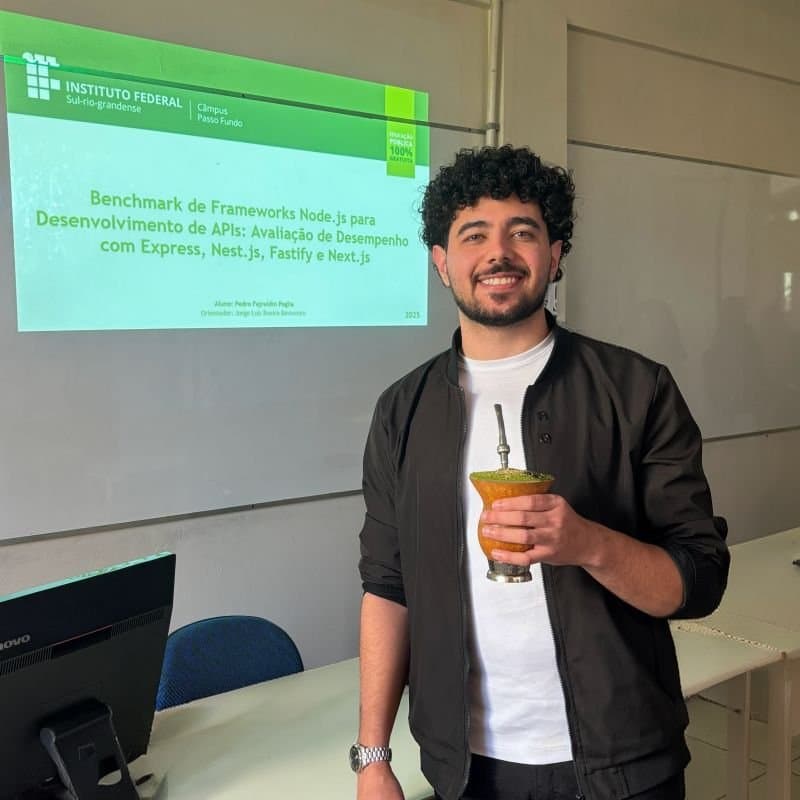 Pedro holding a chimarrão next to the presentation of his Node.js frameworks paper
